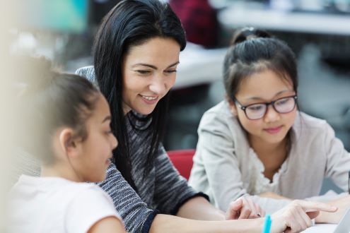 A teacher shows two students something on a laptop