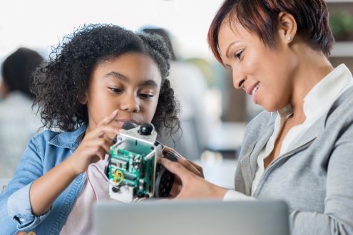 A teacher helps a student program a robot.