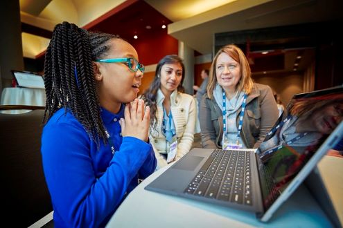 Girl looks at computer screen while educators look on.