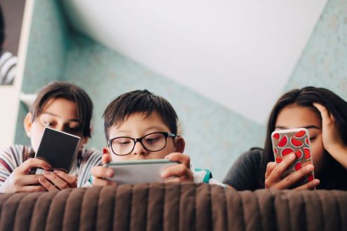 Three teenagers looking at their phones while sitting on a couch