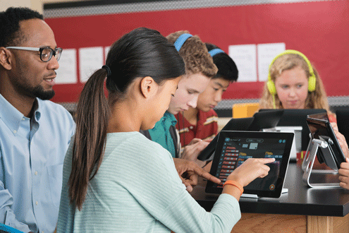 Students use a computer as teacher looks on