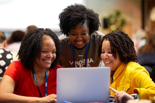 3 edtech coaches smile as they look at a laptop screen