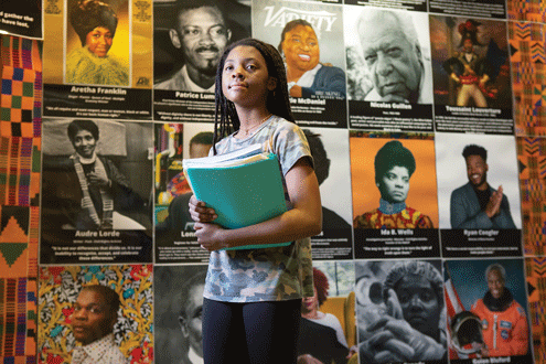a girl stands in front of a display of photos of Black leaders