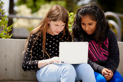 dos niñas leen algo en una computadora portátil