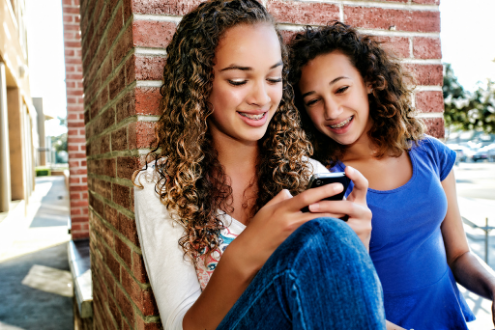 two girls smile while looking at phone screen