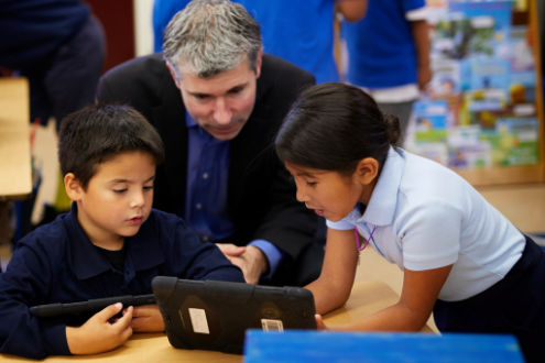 Dos estudiantes y un maestro trabajan en una computadora portátil.
