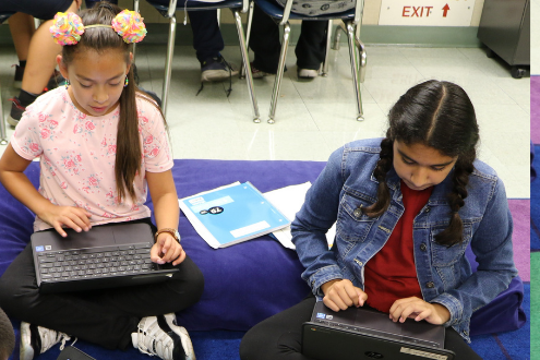 two girls sitting on classroom floor with laptops working on coding projects