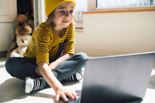 una niña trabaja en una computadora portátil en el piso de su casa