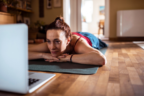 A woman lying on a yoga mat while watching something on a laptop