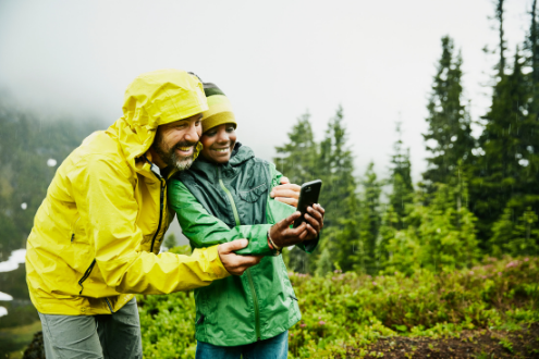 A boy and his dad use cell phone to gather data outside.