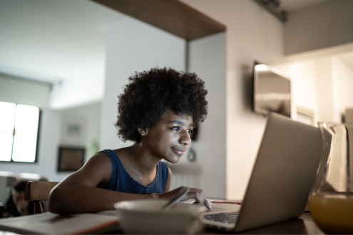 Un estudiante se sienta en su cocina sonriendo a su computadora portátil