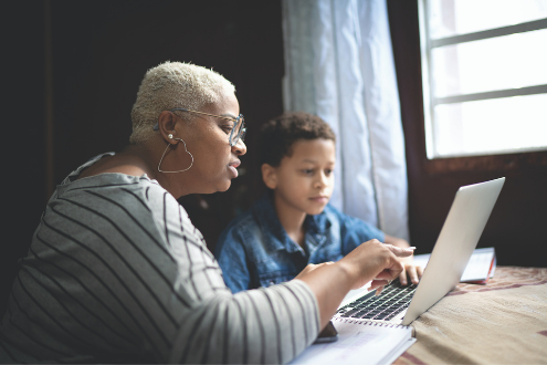 A woman helps a child read something on a laptop