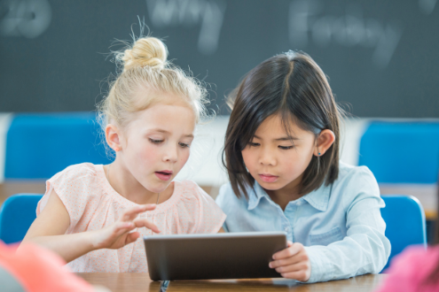 Two young girls play a game on a digital tablet