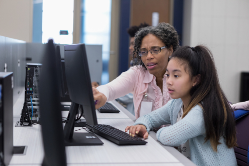 A teacher shows students something on a desktop computer