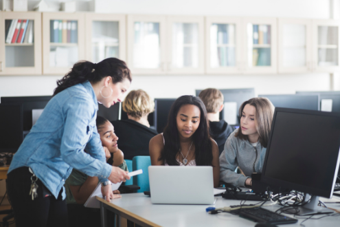 A teacher helps students on a laptop