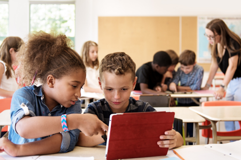 Two students in a classroom work on a tablet computer