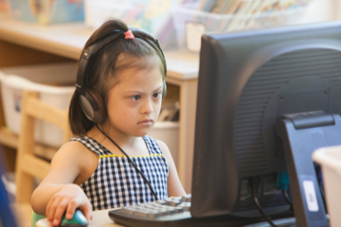 A girl is wearing headphones while using a desktop computer