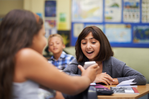 One student smiles as a classmate shows her something on a smartphone