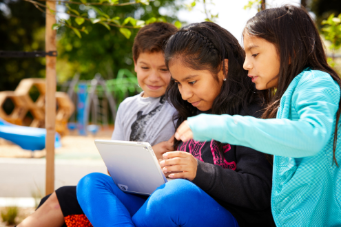 three school children look at something together on a laptop computer