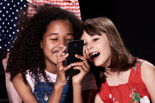 two students smile excitedly as they look at a phone