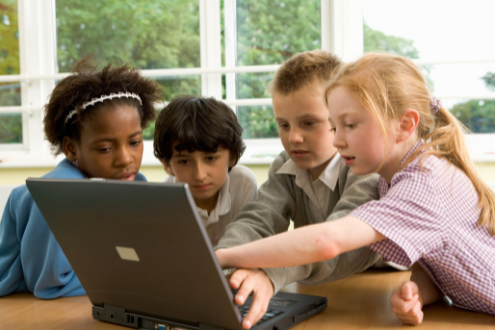 A group of four school children work together at a laptop