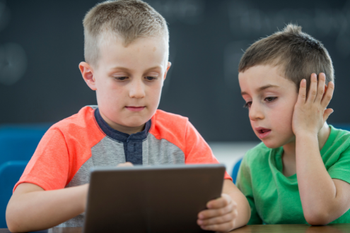 two elementary school boys watch a video on on iPad