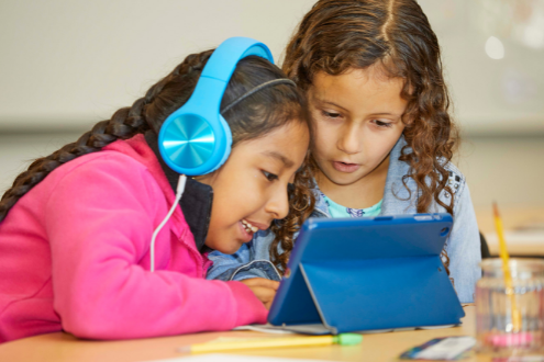 Two girls listen to content on a shared iPad