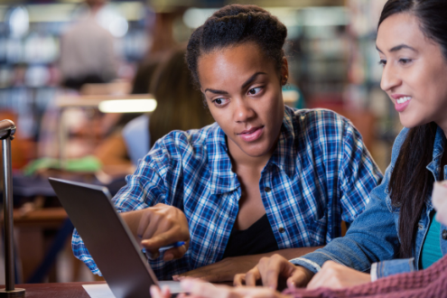 Dos chicas adolescentes estudian algo en una computadora.