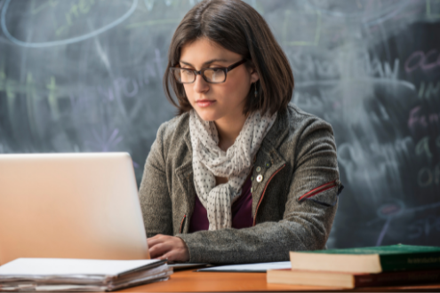 a teacher at her desk looking at a laptop research tools