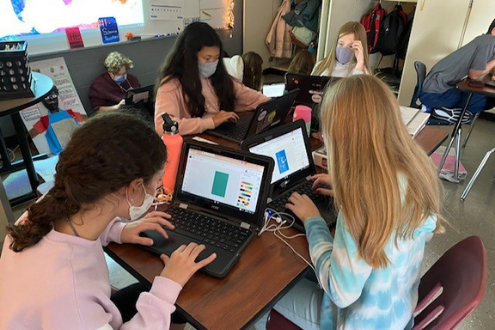 Un grupo de estudiantes colabora usando sus computadoras portátiles de la escuela.