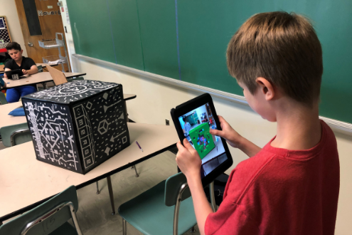 a boy uses an ipad to scan a merge cube
