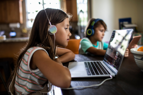 a girl listens to headphones while studying Spanish at a laptop