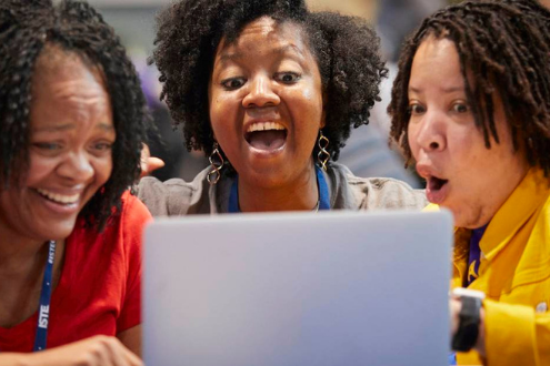 3 educators sit around a laptop with surprised faces