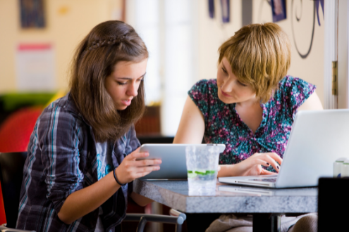 Two girls work on a project over a laptop