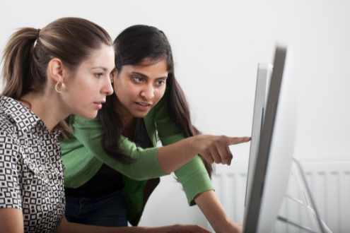 An edtech coach points to something at a computer screen while a teacher follows along.