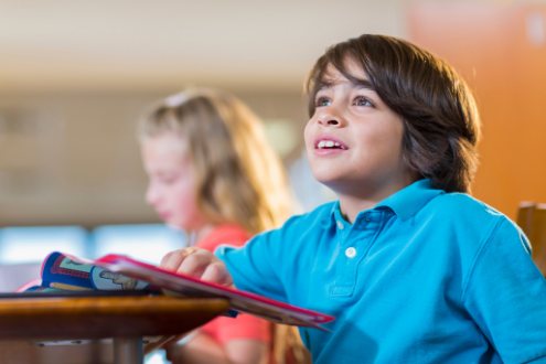 A boy sitting at a school desk gazes upward. 