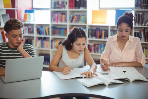 Three students at a school library table working on a laptop.