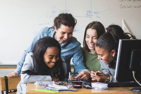 A teacher surrounded by three students working on a robotics project