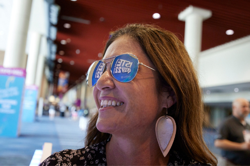 Una mujer sonríe mientras usa anteojos de sol que reflejan el logo de ISTELive 22 en el Centro de Convenciones de Nueva Orleans.