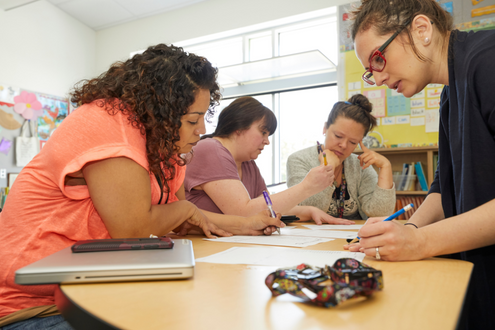 Four elementary school teachers sit around a group of tables at a school and work on lesson planning