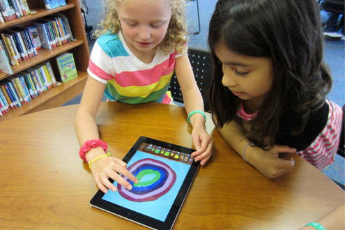 Two children in a school library doing art on an iPad during Dot Day