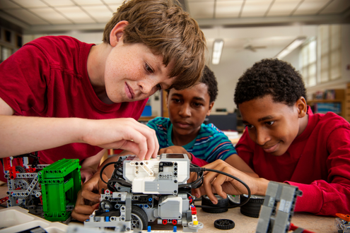 Three boys work on building a robotics project together