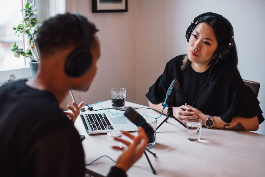 A woman and a man sitting at a table recording a podcast.