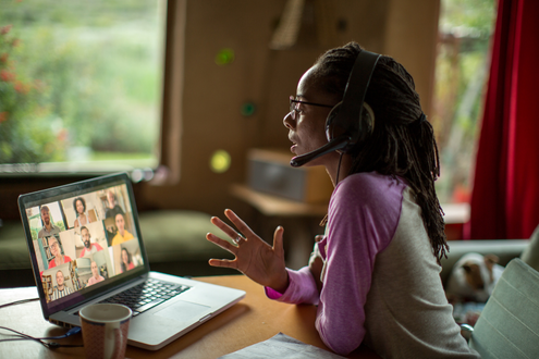 a teacher in front of a laptop attending a zoom call with many people's faces on the screen.