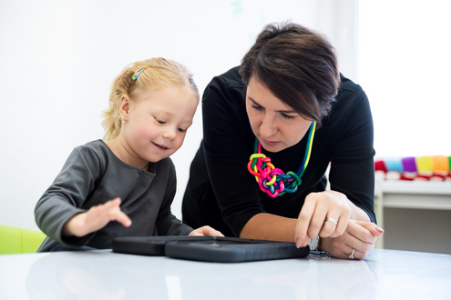 A speech pathologist works with a student using a tablet for a communication device