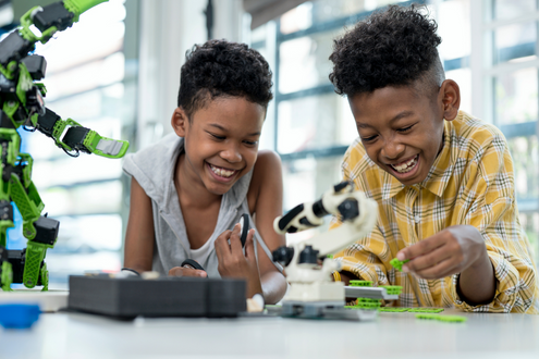 Two smiling students work on a robotics project in school