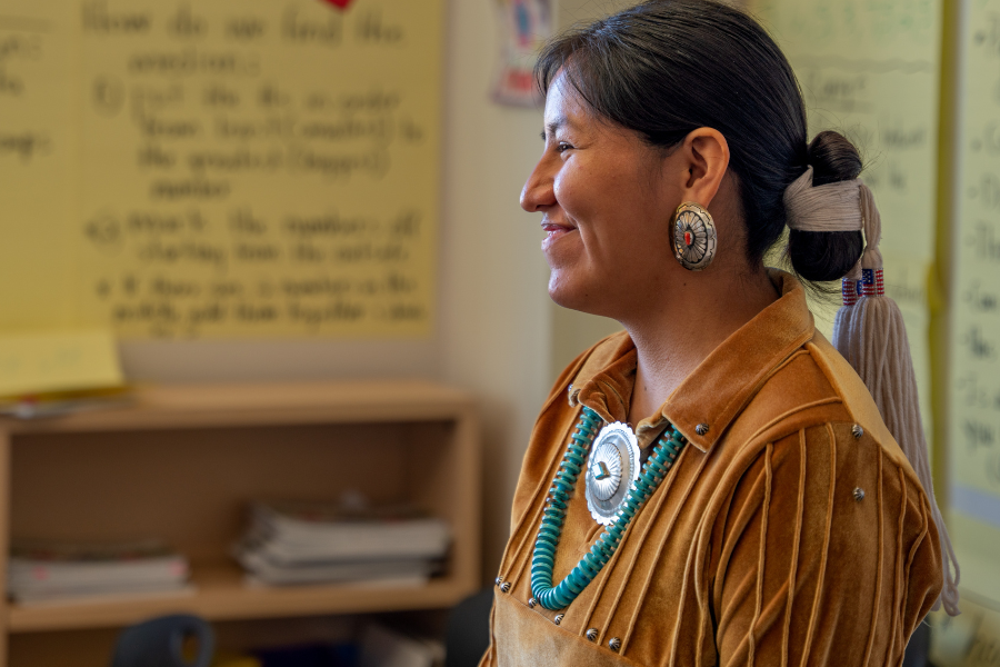A Native American in traditional clothing talks to a class of students.