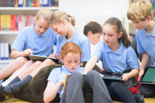 a group of students sitting on soft furniture in a library work together on iPads