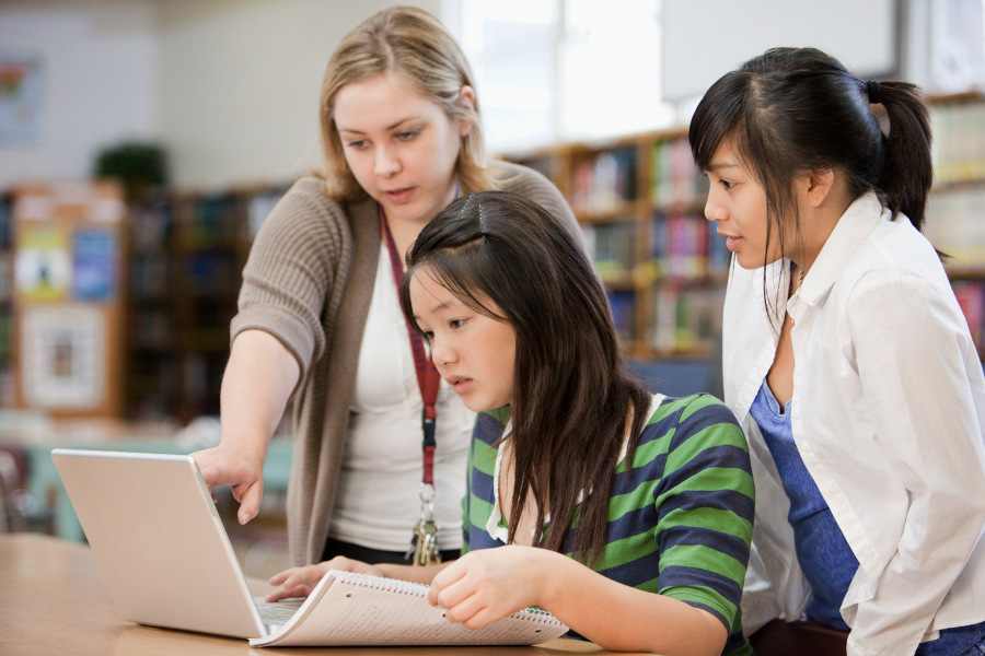 a teacher points to something on a laptop while two students look on