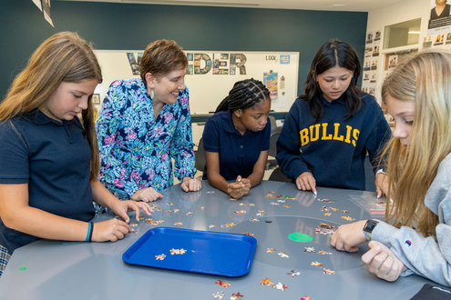 four students and a teacher stand over a table doing a team-building activity